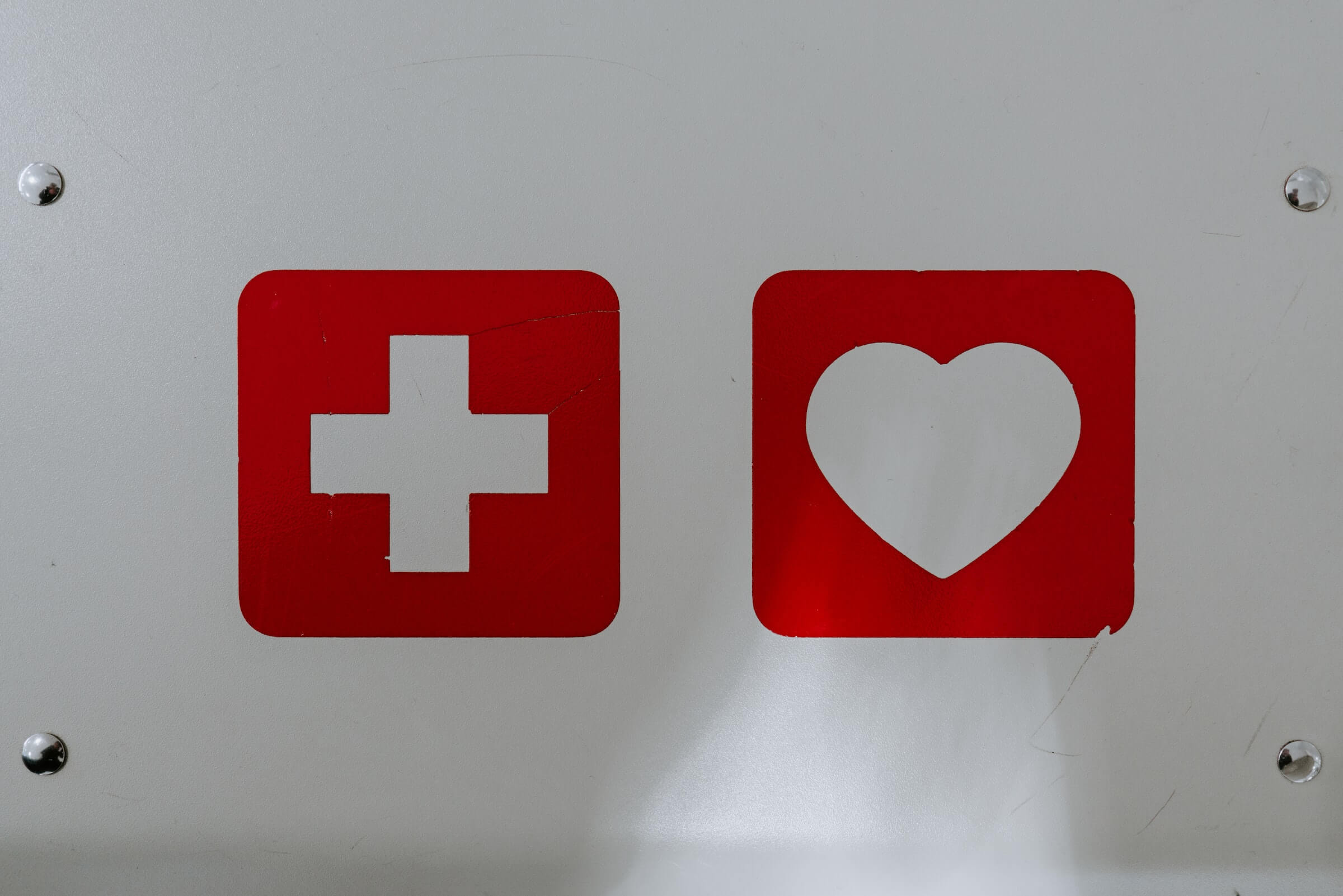 White Cross in Red Square and White Heart in Red Square Next to Each Other on White Background